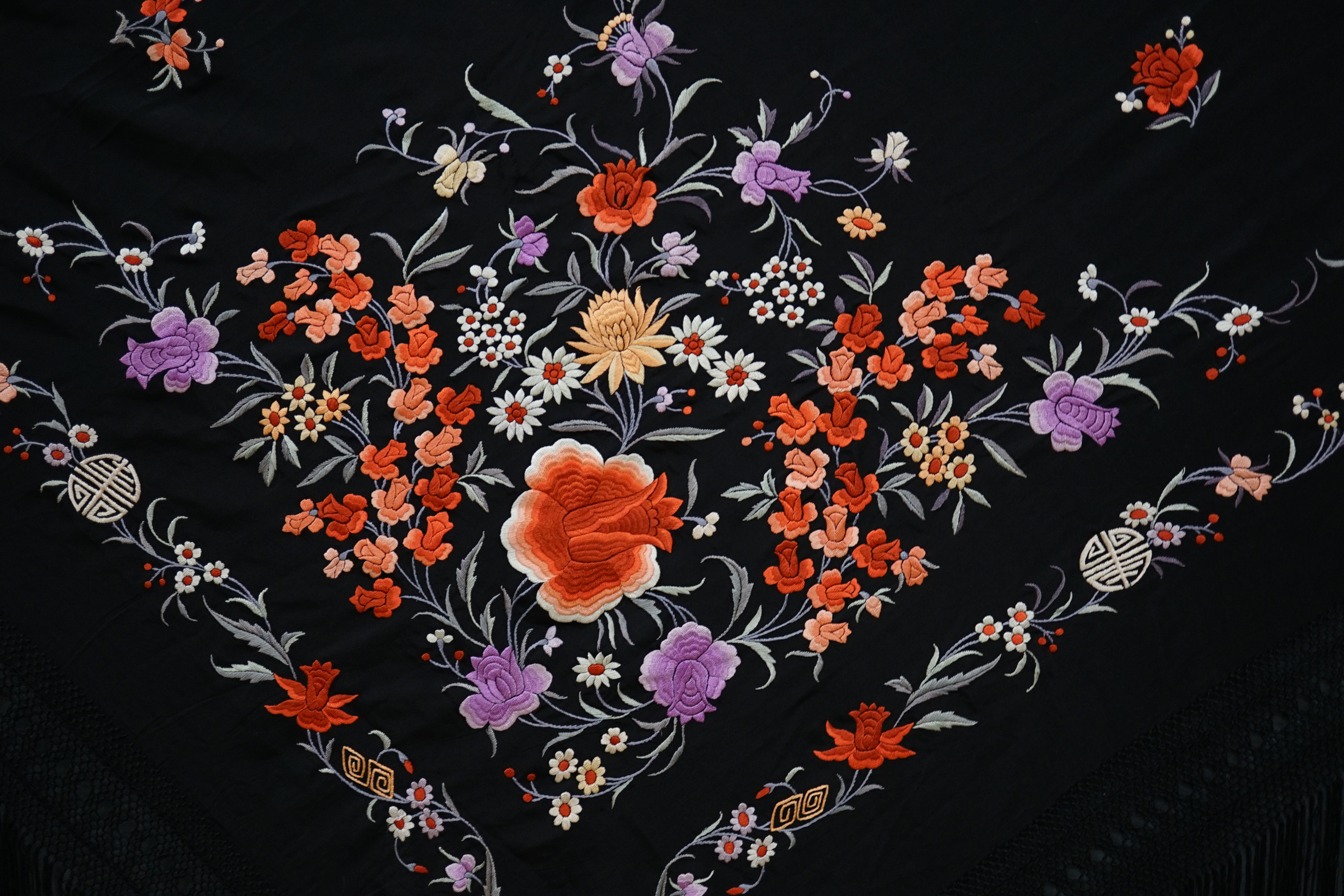 A late 19th / early 20th century Chinese black silk shawl, with polychrome silk embroidered flowers in green, red, orange, lilac, yellow and white, the centre embroidered with, sprigs of multi-coloured flowers, the four